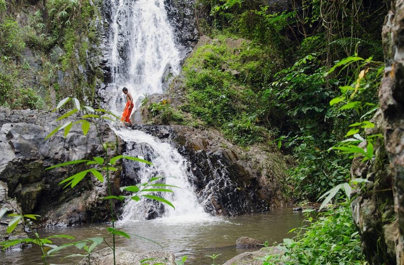 Un monaco attraversa una cascata nel Parco Nazionale di Khao Phanom Bencha
