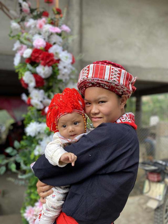 Una madre e il suo bambino, entrambi vestiti con colorati abiti da sposa Hmong